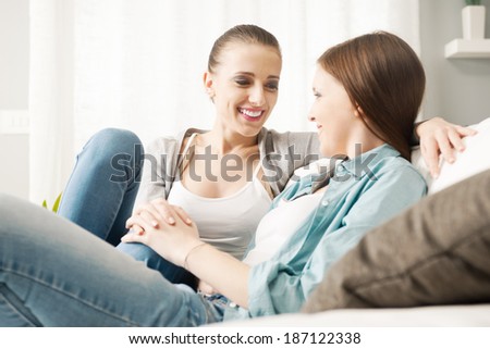 Loving lesbian couple flirting and holding hands on the sofa at home.