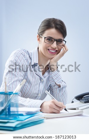 Young attractive businesswoman writing down notes and smiling.