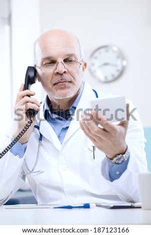 Doctor talking on the phone and looking at medicine\'s box.