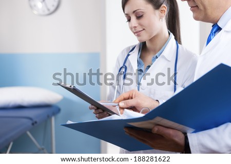 Young female practitioner and senior doctor checking medical records on a clipboard.