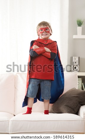 Little superhero boy standing on sofa and posing like a real hero.