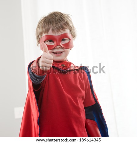 Smiling super hero kid at home with thumb up, looking at camera.