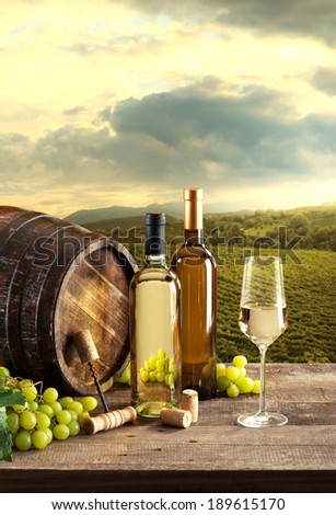 Wine bottles with barrel still life and lush natural landscape on background with vineyards.