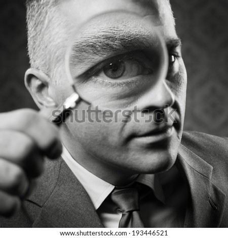 Vintage detective looking at camera through magnifying glass.