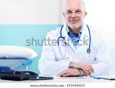 Senior doctor at his desk working with medical equipment in the background.