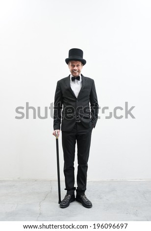 Classy smiling gentleman standing on white background and concrete floor in elegant suit with cane and bowler hat.
