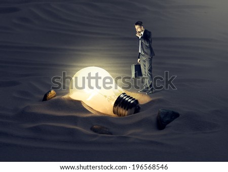 Businessman finding a light bulb in the dark.