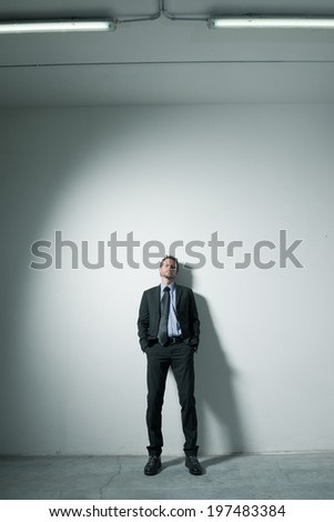Attractive businessman leaning on a wall with hands in pockets and dramatic lighting.