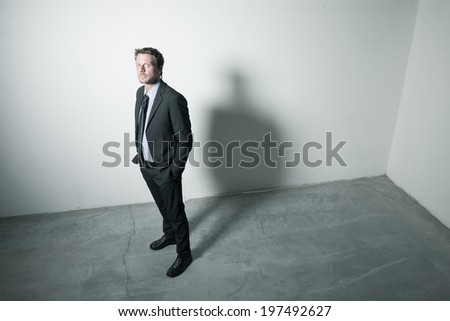 Attractive businessman standing with hands in pockets in an empty room with dramatic lighting.