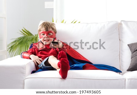Cute boy with super hero costume sitting on living room sofa and watching tv.