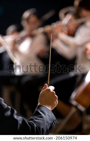 Conductor directing symphony orchestra with performers on background, hands close-up.