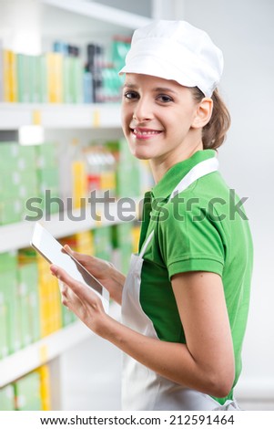 Smiling female sales clerk holding a digital tablet at supermarket.