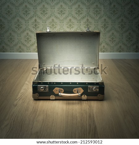 Open vintage suitcase on wooden floor with vintage wallpaper on background.