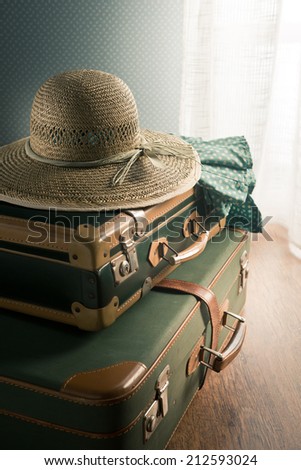 Vintage suitcase with straw hat on the floor next to a window.