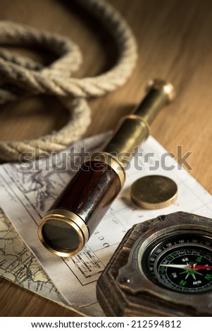Old map with brass telescope, compass and rope on background.