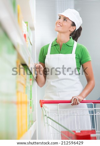 Smiling young saleswoman with shopping cart at supermarket.