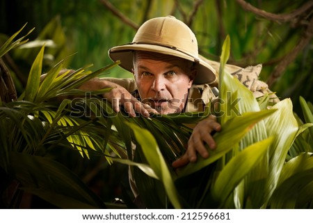 Adventurer hiding and peeking through plants in the rainforest jungle with exploration equipment.