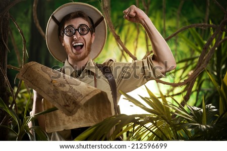 Young smiling explorer in the jungle with thick glasses and fist raised holding a map.
