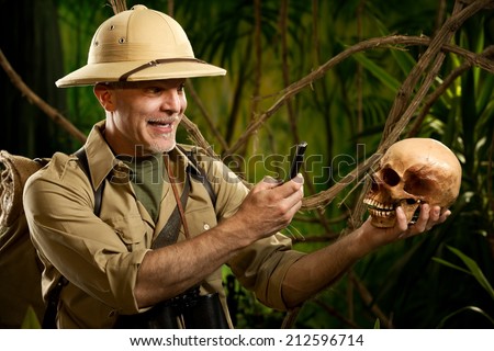 Smiling explorer taking a picture of a skull in the jungle with a mobile phone.