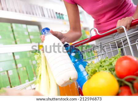 Full shopping cart at store with fresh vegetables and hands close-up.