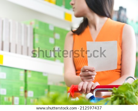 Young woman holding a shopping list an searching products on shelves.