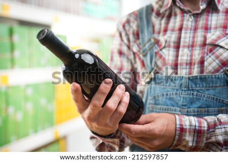 Farmer holding a wine bottle at supermarket and reading label.