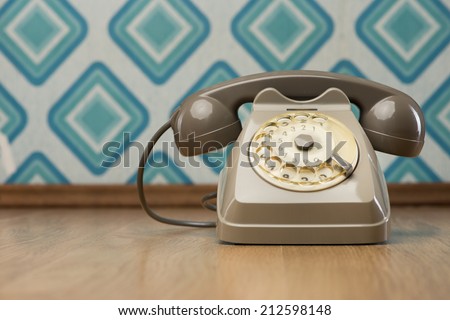 Vintage gray telephone on hardwood floor, diamond light blue retro wallpaper on background.