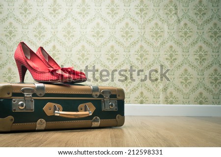 Female red dotted shoes with vintage suitcase on floor and retro wallpaper.