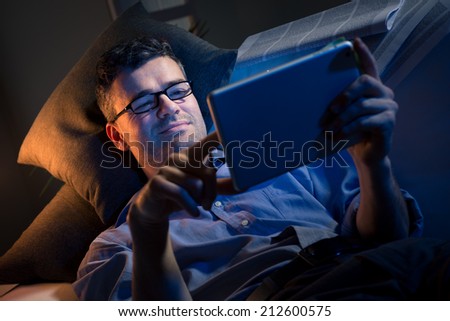 Man working at night lying down on sofa in the living room with tablet.