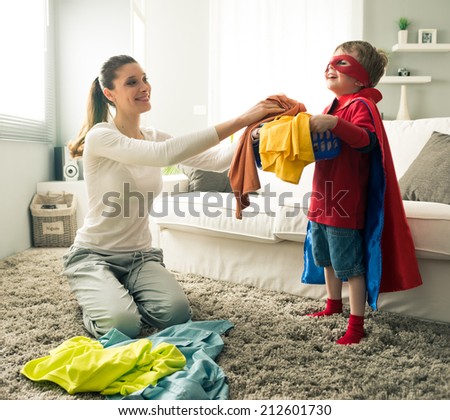Superhero boy and his mother doing laundry together in the living room.