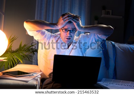 Shocked businessman with head in hands staring at laptop screen late at night.