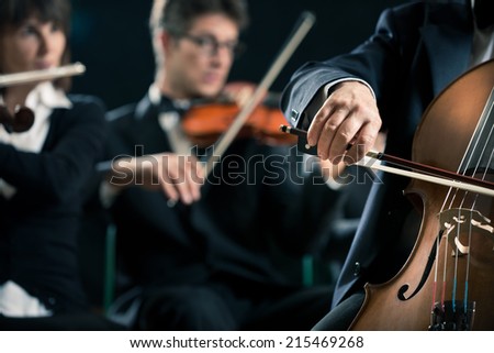 Symphony orchestra performing with cello player hand close-up.