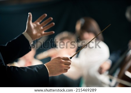 Orchestra conductor directing symphony orchestra with performers on background, hands close-up.