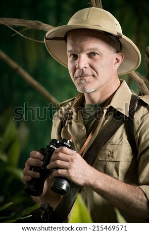 Smiling explorer in colonial style clothing holding binoculars and looking at camera.
