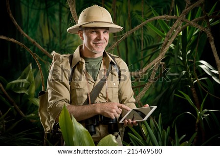 Smiling adventurer in the jungle holding a digital tablet.