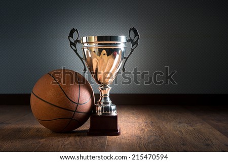 Basket ball and gold bright trophy on hardwood floor.