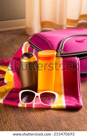 Sun protection cosmetics and sunglasses on striped towel next to a bag.