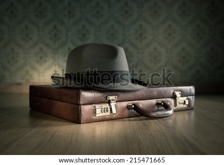 Borsalino hat on leather vintage briefcase on wooden surface with vintage wallpaper on background.