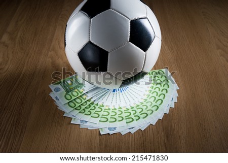 Soccer ball with fan of euro banknotes on hardwood floor.