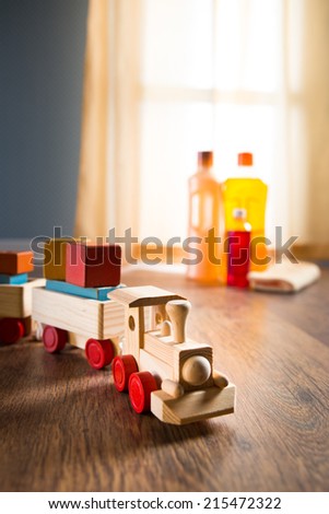 Wooden toy train with wood cleaner products on parquet next to a window.