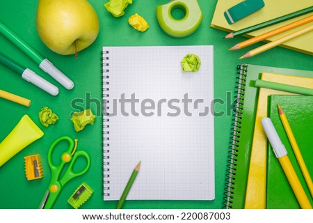 Back to school with notebook, green stationery and apple on desktop.