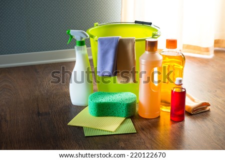 Wood cleaners and detergents on floor with bucket, gloves, cloth and sponges.