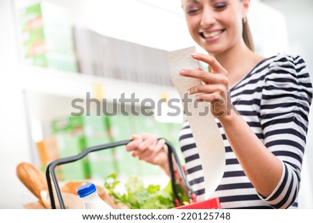 Smiling young woman holding a long grocery receipt at supermarket.