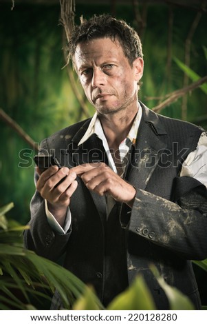 Lost businessman in torn clothing using mobile phone in the jungle.