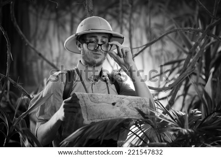 Young confident explorer in the jungle examining an old map and adjusting glasses.