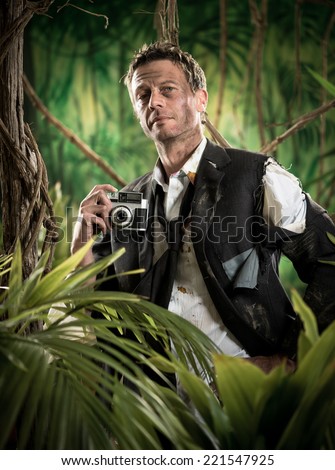 Attractive man in torn clothing walking in jungle with vintage camera.