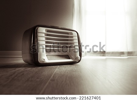 Vintage radio next to a window with curtain on hardwood floor.