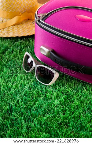 Sunglasses, straw hat and pink bag on perfect lush grass, leaving for vacations concept.