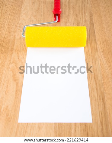 Yellow and red paint roller on hardwood floor with white copyspace paint.