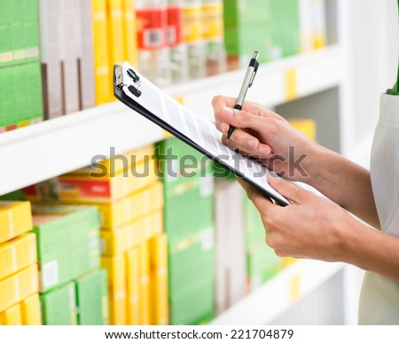 Supermarket clerk at work holding pen and clipboard with shelf on background, hands close-up.